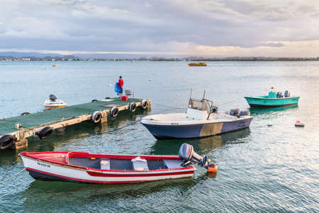 San Juan, Puerto Rico - April 30, 2019: Fishing boats moored near the shore of San Juan, Puerto Rico, Caribbean. A lone fisherman stands on a pier with a fishing net during the sunset.のeditorial素材