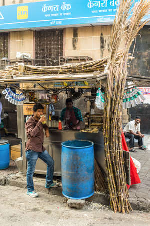 Mumbai, India - November 22, 2019: Unidetified local man drinks sugarcane juice on the street in Mumbai, India. Mumbai is famous for its street food. Stalls offer delightful variety of meals.のeditorial素材