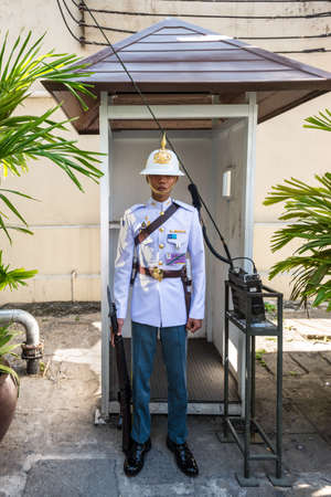 Bangkok, Thailand - December 7, 2019: Soldier of the royal guard in patent leather with a radio station nearby at the Royal Grand Palace in Bangkok, Thailand.のeditorial素材