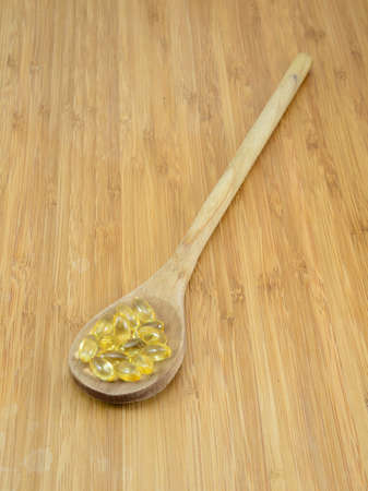 Yellow vitamin pills in a wooden spoon against a bamboo background の写真素材