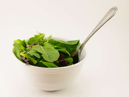 Mixed Salad Greens in a White bowl with fork isolated on a white backgroundの写真素材