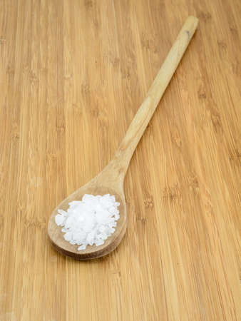 Sea salt crystals in a wooden spoon against a bamboo background の写真素材