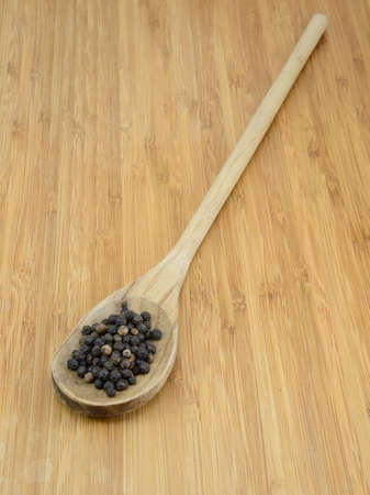 Black pepper in a wooden spoon against a bamboo background の写真素材