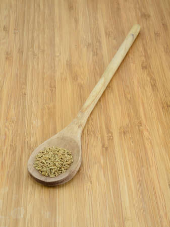 A pile of cumin seeds in a wooden spoon against a bamboo backgroundの写真素材