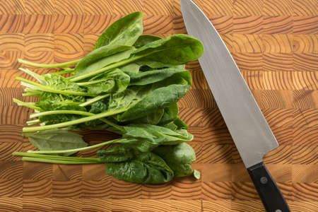 A bunch of spinach on a wooden cutting board with a knife.の写真素材