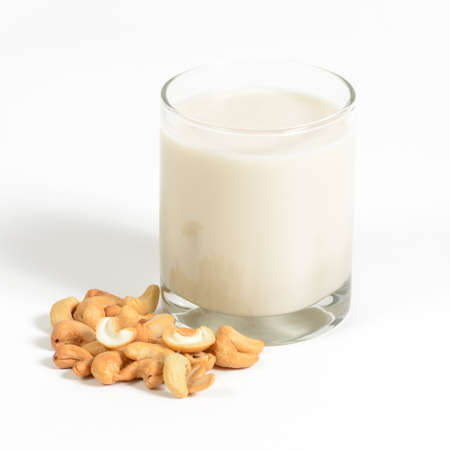 Cashew milk in a glass with cashews on a white background.の写真素材
