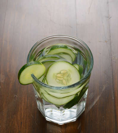 A glass filled with slices of cucumber and water on a wood table.の写真素材