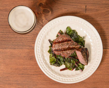 A grilled filet mignon steak on a bed of swiss chard with a glass of beer.の写真素材