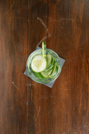 A glass filled with slices of cucumber and water on a wood table.の写真素材