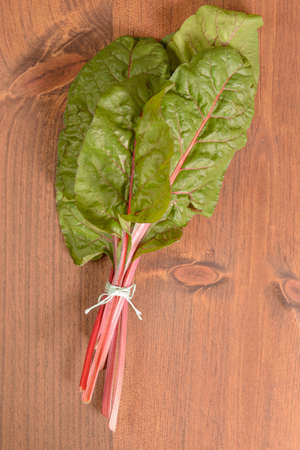 A bunch of swiss chard tied together on a wood table.の写真素材