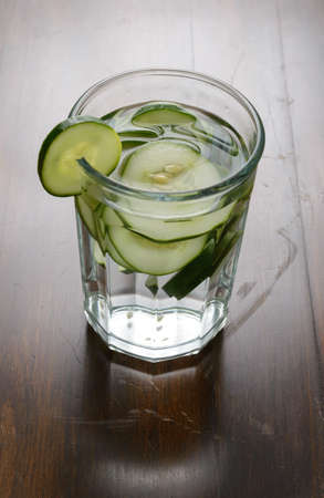 A glass filled with slices of cucumber and water on a wood table.の写真素材