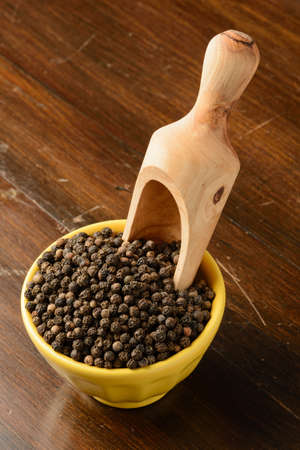 Black peppercorn in a yellow bowl with a wooden scoop.の写真素材