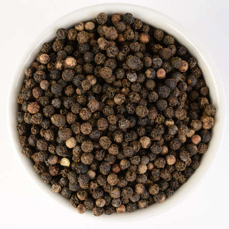 Black peppercorn in a white bowl isolated on a white background.の写真素材