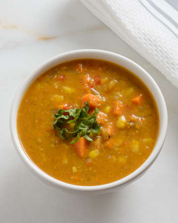 Warm sweet potato and corn soup in a white bowl on a marble backgroundの写真素材