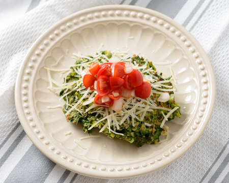 Pan fried spinach fritters platted and topped with cherry tomatoes and shredded cheese.の写真素材