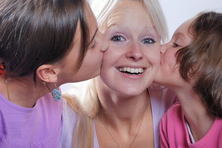 A mother smiles as she receives a kiss on the cheek from her young daughtersの写真素材