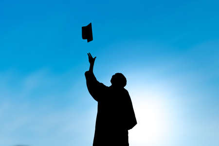 Graduates throwing hat on graduation day, silhouette with blue skyの写真素材