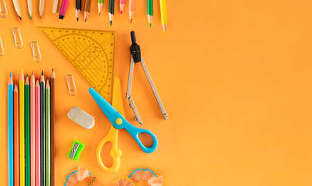 Top view of school supplies on an orange background. Creative chaos on the school desk with copy...
