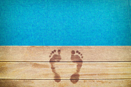 :icture of footprints on the wooden surface with blue swimming pool on the background.