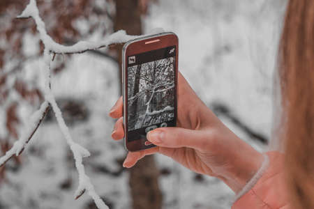 Young girl taking winter nature pictures with mobile phone in the forestの写真素材