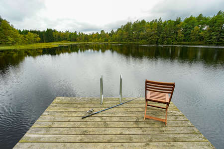Fishing equipment on seat on lake. Feeder carp rods on wooden pier.の写真素材