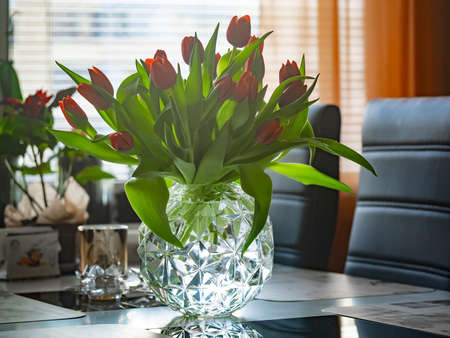 Glass vase with red tulips flowers in light cozy interior. White table and light from the windowの写真素材
