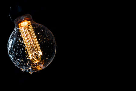 Warm colored and glowing bulb with water drops on a dark background.の写真素材
