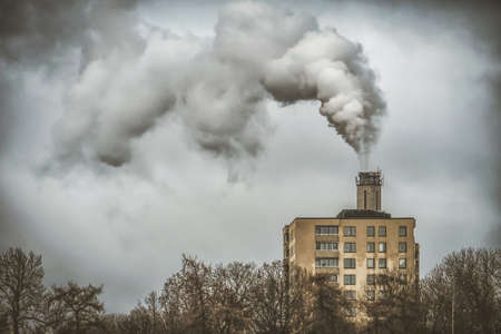 The plant emits pollutants into the atmosphere, from the factory pipes comes out a thick smoke behind the apartments buildingの写真素材