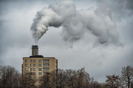 The plant emits pollutants into the atmosphere, from the factory pipes comes out a thick smoke behind the apartments buildingの写真素材
