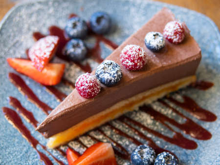 Slice of chocolate cheesecake with strawberries, blueberries and raspberries on the blue plate with chocolate sauce, above view over a rustic wood backgroundの写真素材