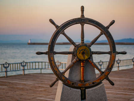 Captains steering wheel or rudder of an old wooden sailing ship in a port at sunsetの写真素材