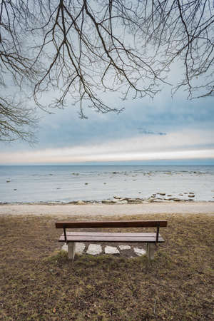Lonely wooden bench on the autumn sea with cloudy skyの写真素材