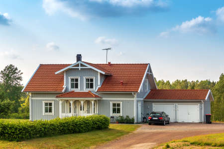 Beautiful scandinavian style house with two places garage and gar in fron of it. Summer with blue scky and green grassの写真素材