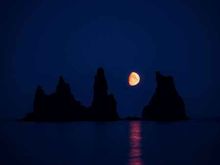 Silhouette of basalt rock formations Troll Toes on Black beach at noght with moon between the rocks. Reynisdrangar, Vik, Icelandの写真素材