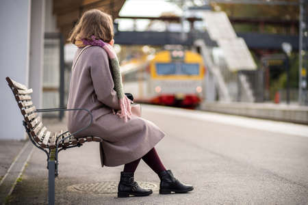 Picture of Young woman sitting on the bench waiting for the train. Autumn seasonの写真素材