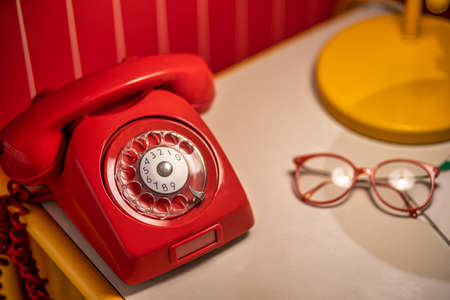 Old red telephone with rotary dial on the table with old glassesの写真素材