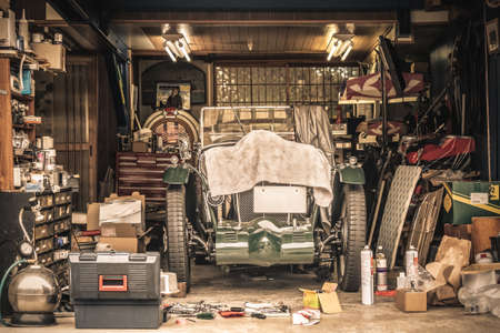 Retro vintage car covered by white cloth. Renovation project in the garage with lots of mechanical details and toolsの写真素材