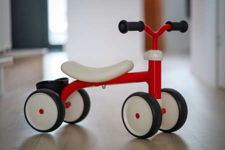 Plastic red four wheeled child bicycle on the wooden floor