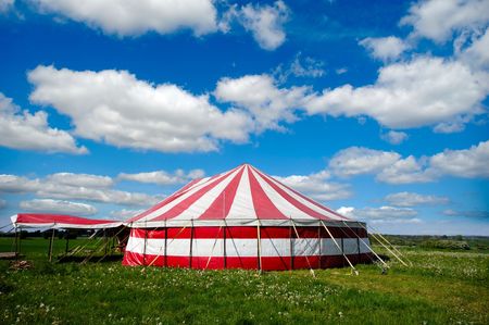 A red and white striped circus tent in green nature. The sky is blue with white cumulus cloudsの写真素材