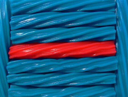 A closeup/macro photograph of one red licorice twist surrounded by several blue ones.の写真素材