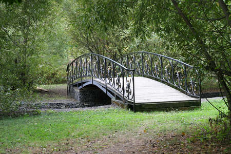 Small delicate wooden arched bridge over a quiet stream deep in the old, thick holiday Park.の写真素材