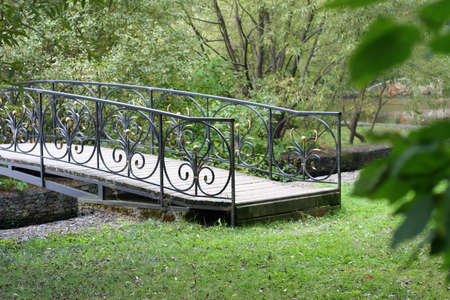 Small delicate wooden arched bridge over a quiet stream deep in the old, thick holiday Park.の写真素材