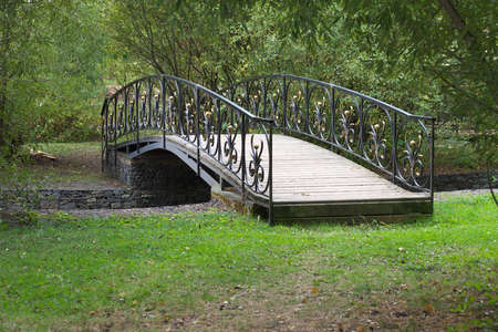 Small delicate wooden arched bridge over a quiet stream deep in the old, thick holiday Park.の写真素材