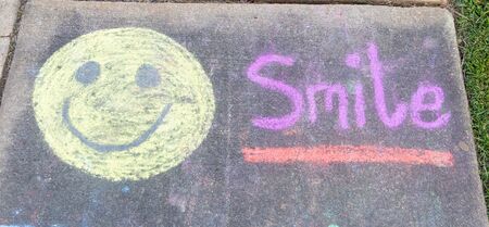 the word "Smile" amd a smiley face written with sidewalk chalk on gray concrete pavement backgroundの写真素材