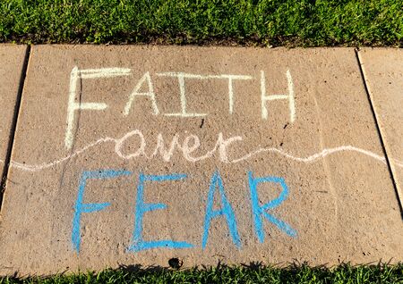 The words "Faith over Fear" written with sidewalk chalk on gray concrete pavement background.の写真素材