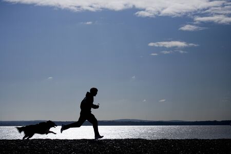 Man running with dog on beach silhouetteの写真素材