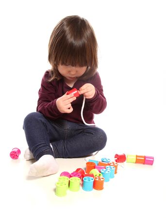 two year old girl playing with cotton reels in studioの写真素材
