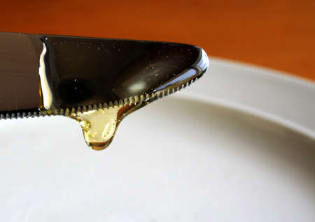 A honey drop, dripping from a knife.の写真素材
