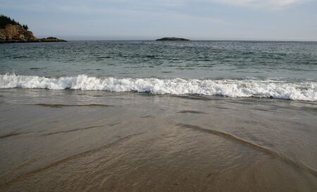 Waves breaking as they reach the sandy shore.の写真素材