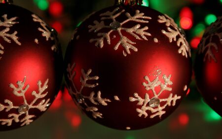 Three red snowflake baubles with red and green christmas lights in the background.